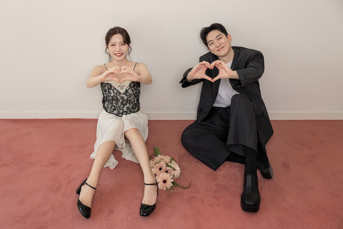 붉은 바닥에 앉아 손하트를 만드는 두 사람